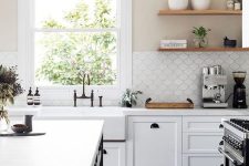 a stylish white farmhouse kitchen with a black kitchen island, white stone countertops and a white scallop tile backsplash