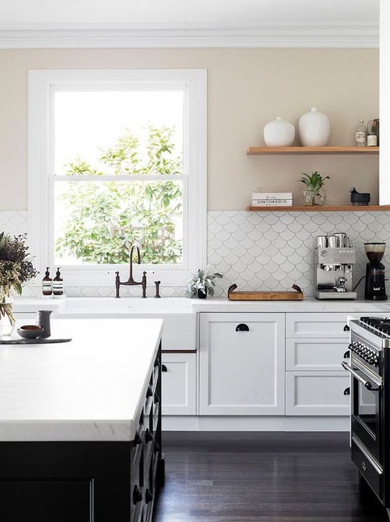 a stylish white farmhouse kitchen with a black kitchen island, white stone countertops and a white scallop tile backsplash