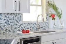 a stylish white kitchen with shaker cabinets, an eye-catchy blue, grey and white fishscale tile backspalsh and stainless steel appliances