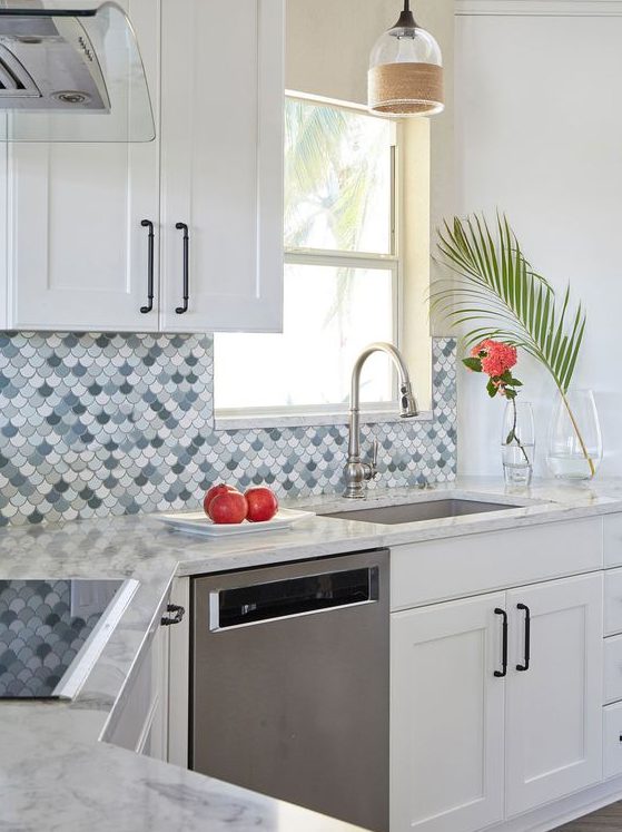 a stylish white kitchen with shaker cabinets, an eye-catchy blue, grey and white fishscale tile backspalsh and stainless steel appliances