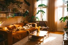 a sun-filled living room with greige walls, a rust-colored sofa, a neutral rug, a tiered coffee table and potted plants