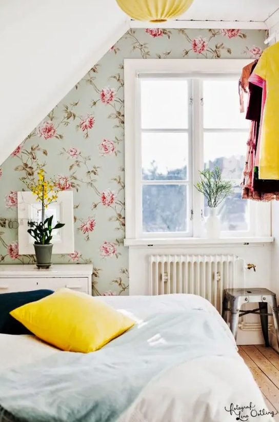 a sweet attic bedroom with a pretty floral wallpaper accent wall, white furniture and a makeshift closet is lovely and cool