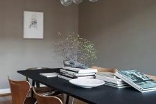 a taupe Scandinavian dining room with a black table, plywood chairs, a bubble chandelier and some coffee table books