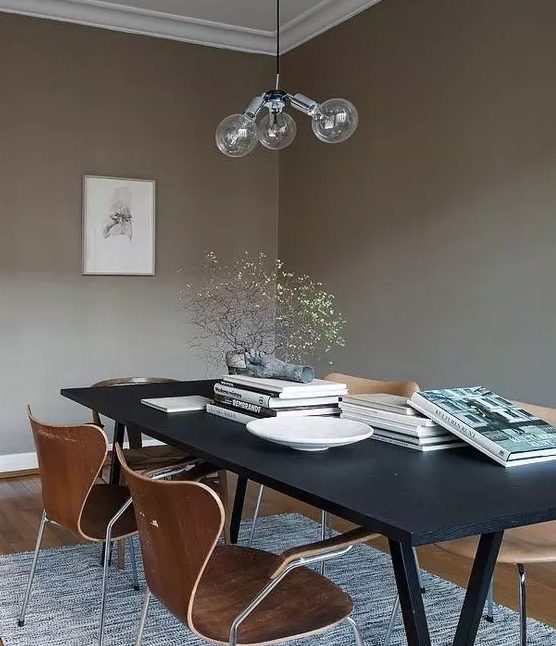 a taupe Scandinavian dining room with a black table, plywood chairs, a bubble chandelier and some coffee table books