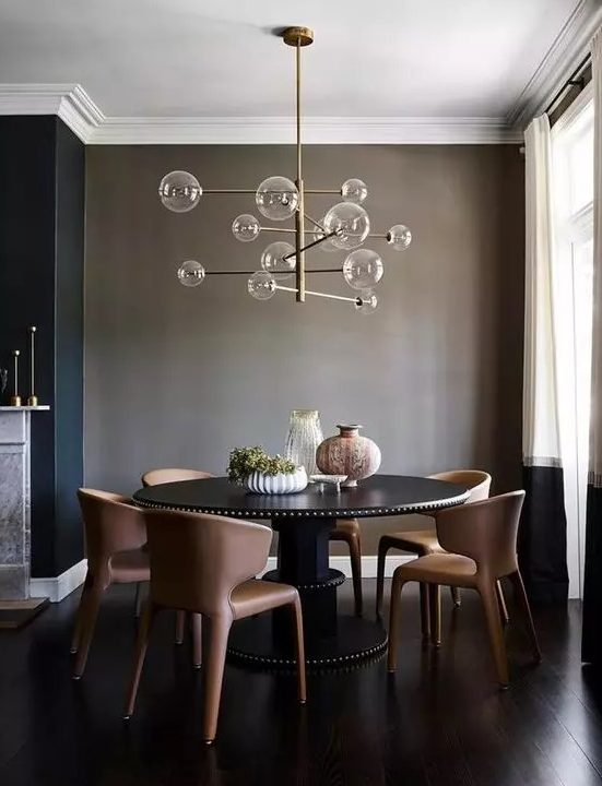 a taupe dining space wiht a large round table in black, chocolate-colored leather chairs and a catchy bubble chandelier