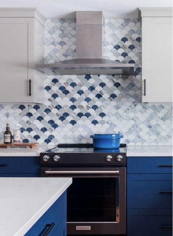 a two-tone kitchen with grey and bold blue cabinets, white stone countertops, an eye-catchy grey, white and navy fish scale tiles
