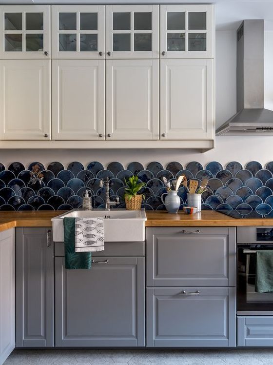 A two tone kitchen with white and grey cabinets, butcherblock countertops, a navy scallop tile backsplash is a cool and catchy solution
