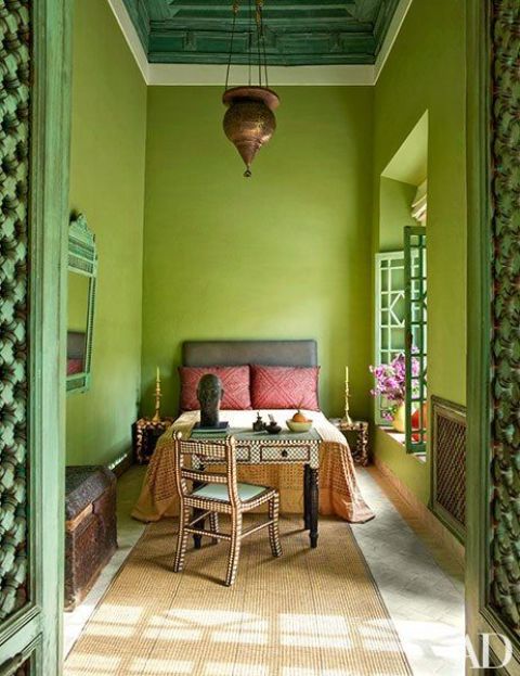 A unique chartreuse Marocco inspired bedroom with a grey bed and colorful bedding, a metal pendant lamp and a desk with a chair
