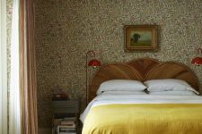a vintage bedroom with floral wallpaper, a bed with a wooden headboard, neutral and yellow bedding, nightstands and red lamps
