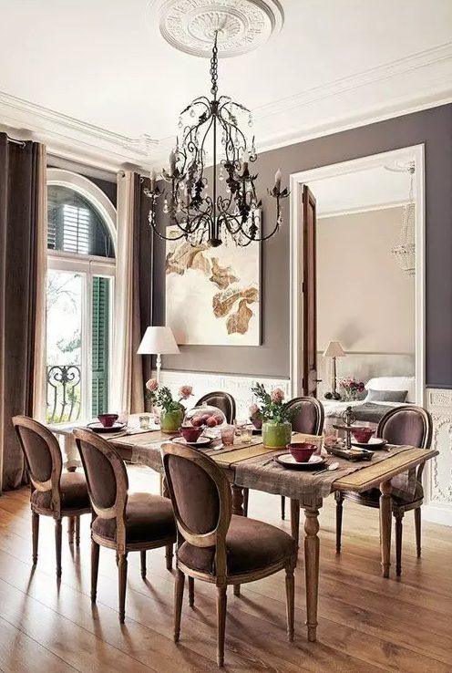 a vintage-inspired taupe dining zone with creamy paneling, a vintage table and taupe chairs, a chic chandelier and some art plus shutters on the window