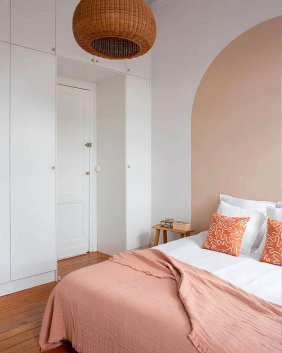 a welcoming bedroom with built-in storage units, a bed with a peachy blanket, stools, a woven pendant lamp and an accent wall