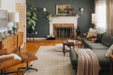a welcoming earthy living room with a dark green accent wall, a fireplace, a green sctional, a brown chair and some plants