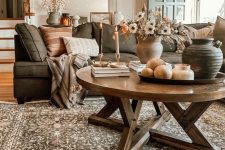 a welcoming earthy living room with a grey sofa and earhty pillows, a printed rug, a stained round table and some candles