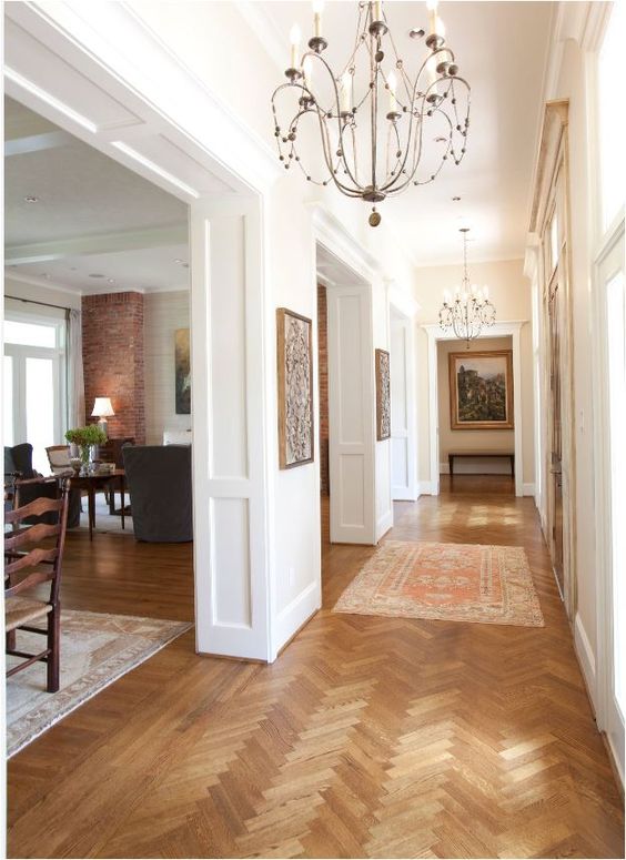 A welcoming space with white molded walls, stained herringbone floors, dark stained furniture and chic chandeliers