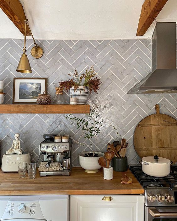 a white farmhouse kitchen with a grey herringbone backsplash, an open shelf, some decor and brass sconces