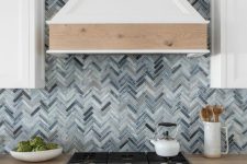 a white farmhouse kitchen with shaker cabinets, a grey herringbone tile backsplash, a hood