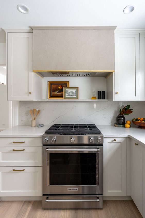 a white farmhouse kitchen with shaker cabinets, a grey hood and some decor under it is a cool and catchy touch of color