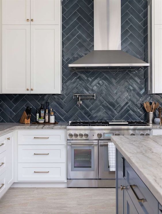 a white farmhouse kitchen with shaker cabinets, grey stone countertops, a navy herringbone tile backsplash and stainless steel appliances