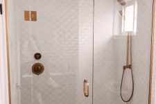 a white shower space clad with fishscale tiles and with a window for natural light plus copper fixtures