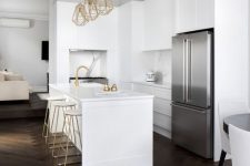 a white sleek kitchen with dark-stained herringbone floors, gold touches and some built-in appliances