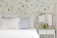 an English cottage bedroom with lovely pastel floral wallpaper, a bed with white and pastel blue bedding, a white nightstand and a mirror