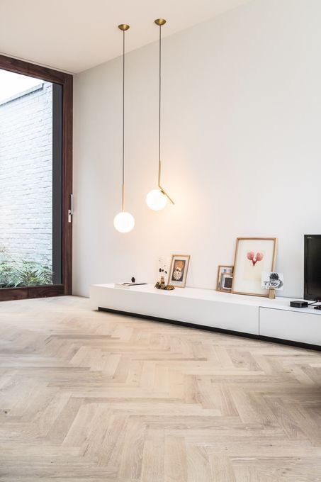 An airy Scandi space with light stained herringbone floor, a white TV unit and some decor and pendant lamps