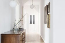 an airy entryway with white walls, light-stained herringbone floors, a vintage stained sideboard and a gallery wall