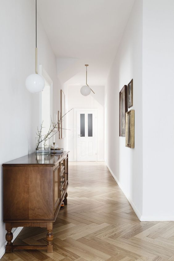 An airy entryway with white walls, light stained herringbone floors, a vintage stained sideboard and a gallery wall
