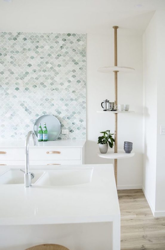 an airy white kitchen with a large aqua, white and green fish scale tile backsplash and white countertops is lovely