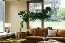 an earthy living room with neutral and a light green wall, a bold printed rug, a green tufted saybed and a mustard sofa