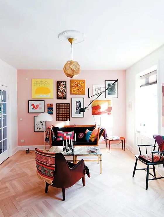 an eclectic living room with a peachy accent wall, a bright free form gallery wlal, a loveseat, a coffee table and some chairs