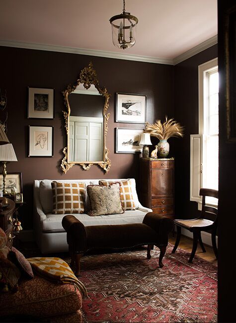 an eclectic living room with brown walls, a white loveseat, printed chairs, a rug and a gallery wall