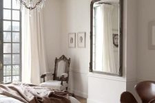 an elegant Parisian bedroom with a herringbone floor, a statement mirror, a chic crystal chandelier and a refined chair