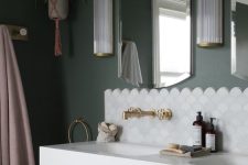 an elegant bathroom with green walls, a blush vanity, a sink, a white scallop tile accent, brass and gold fixtures