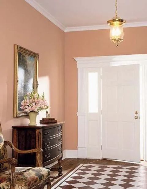 An elegant vintage entryway with Peach Fuzz walls, a dark stained console table, a checked rug and a vintage chair