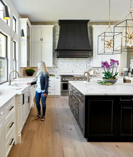 an elegant vintage kitchen with white cabinets, neutral tiles, a large black kitchen island and a matching black hood