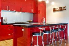 an extra bright red kitchen with black countertops, tall black stools and pendant lamps is a cool space