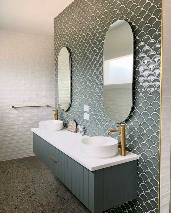 An eye catchy bathroom clad with white tiles and grey green fishscale tiles plus a matching vanity, sinks and gold fixtures