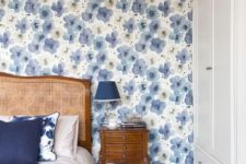 an eye-catchy bedroom with a blue floral accent wall, a stained bed with navy and white bedding, a vintage stained nightstand with a navy table lamp