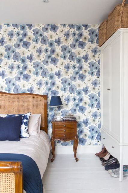 An eye catchy bedroom with a blue floral accent wall, a stained bed with navy and white bedding, a vintage stained nightstand with a navy table lamp