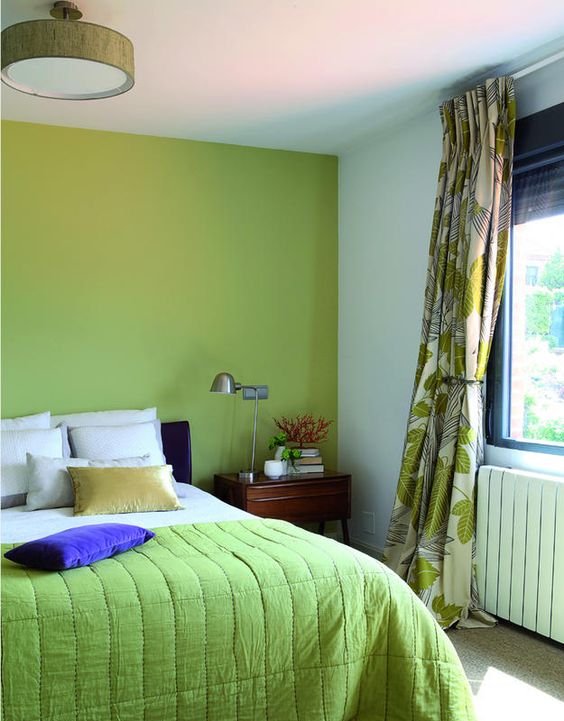 an eye-catchy bedroom with a chartreuse accent wall and a blanket, a bed with neutral bedding, printed curtains