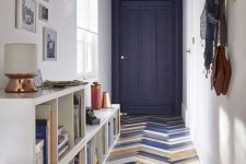an eye-catchy entryway with a bold herringbone floor, a navy door and ceiling, a storage unit and a gallery wall