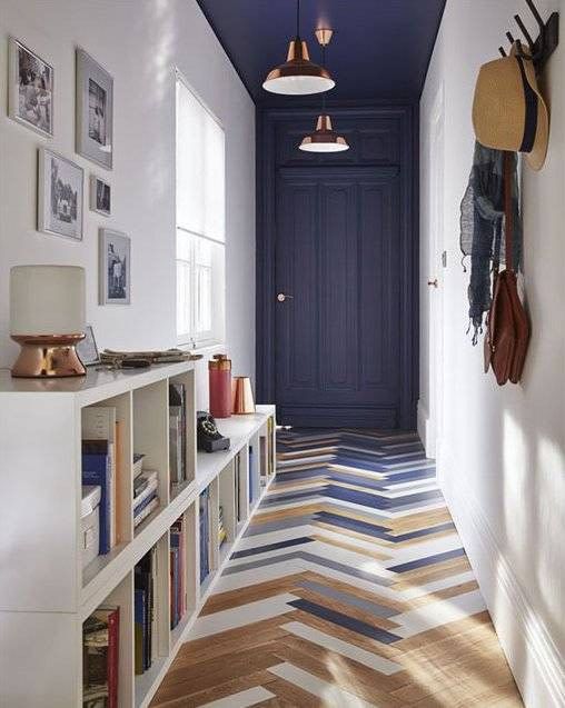 An eye catchy entryway with a bold herringbone floor, a navy door and ceiling, a storage unit and a gallery wall