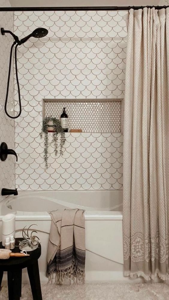 An eye catchy neutral bathroom clad with white fihscale tiles, a niche shelf, black fixtures and neutral textiles