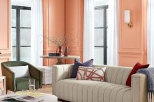 an eye-catchy peach pink living room with paneled walls, a grey sofa, a green chair, a coffee table and neutral curtains
