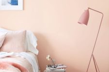 an inviting and warm Peach Fuzz bedroom with a bed with pastel bedding, a pink floor lamp, a stool and a fuzzy rug