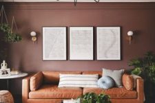 an inviting living room with chocolate brown walls, an amber leather sofa, coffee tables and greenery