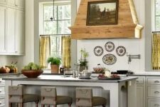an off-white vintage kitchen with shaker cabinets, a stained wood hood with an artwork and yellow curtains