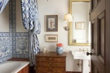a Moroccan bathroom clad with terracotta tiles, with blue ones and blue curtains, a Moroccan pendant lamp and a dark-stained dresser
