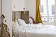 a Paris-inspired chic bedroom with a shutter screen as a headboard, a herringbone floor, mustard curtains and a comfy chair